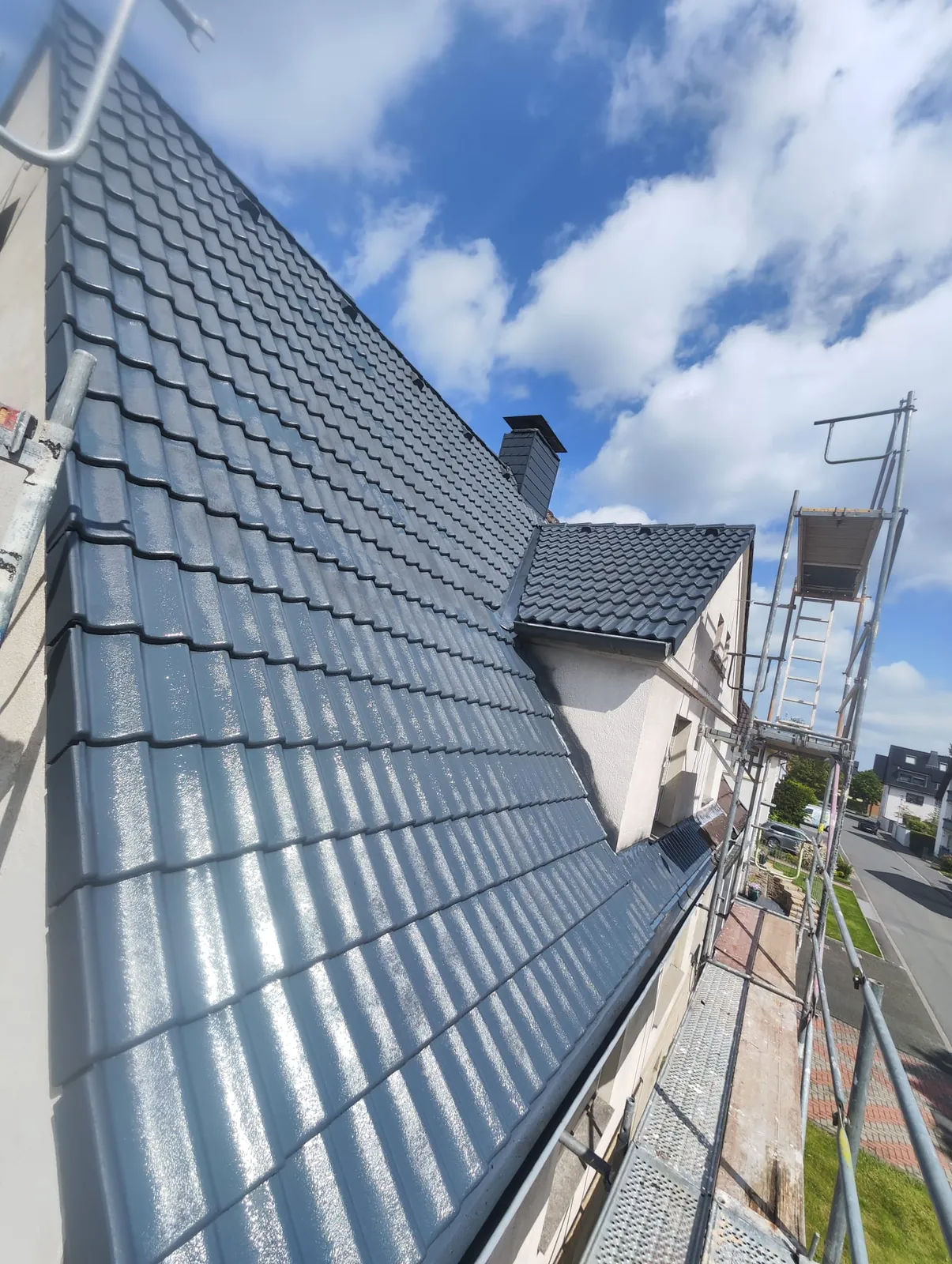 Frisch beschichtete Dachfläche vom Gerüst aus gesehen, glänzendes Anthrazit gegen blauen Himmel